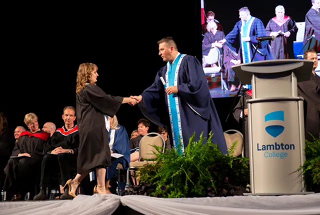 Rob Kardas handing diploma to graduating student on stage.