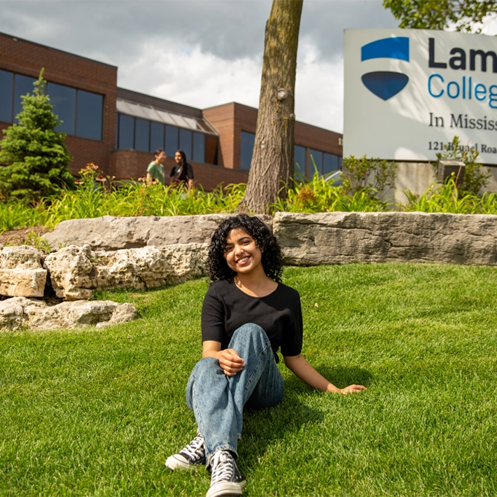 An international student posing for a photo outside of campus sign.