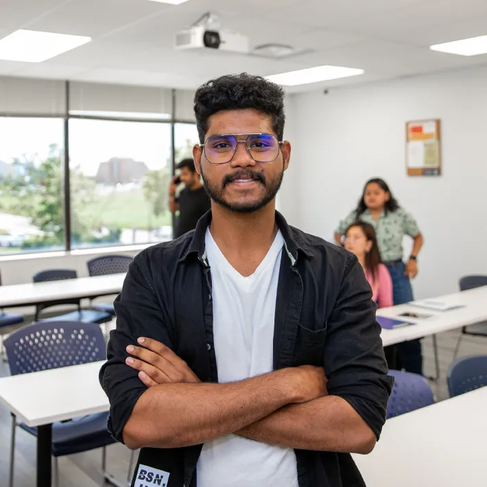An international student posing for photo in a classroom wearing white shirt.