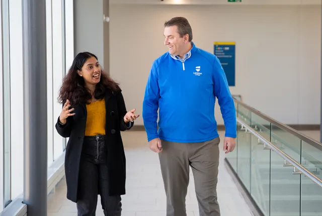 Rob Kardas walking with a student down a campus hallway.