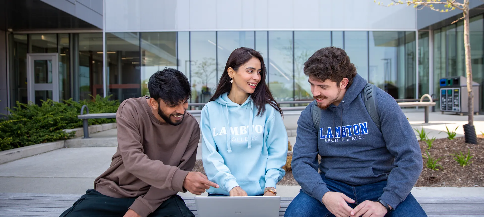 A photo of student sitting out side on campus grounds looking at computer.