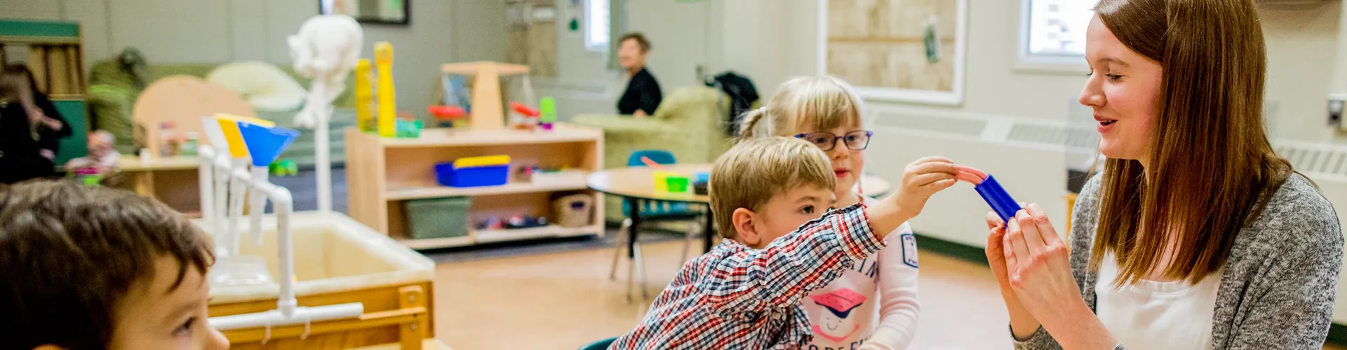 A photo of an EarlyON educator showing children toys at the centre.