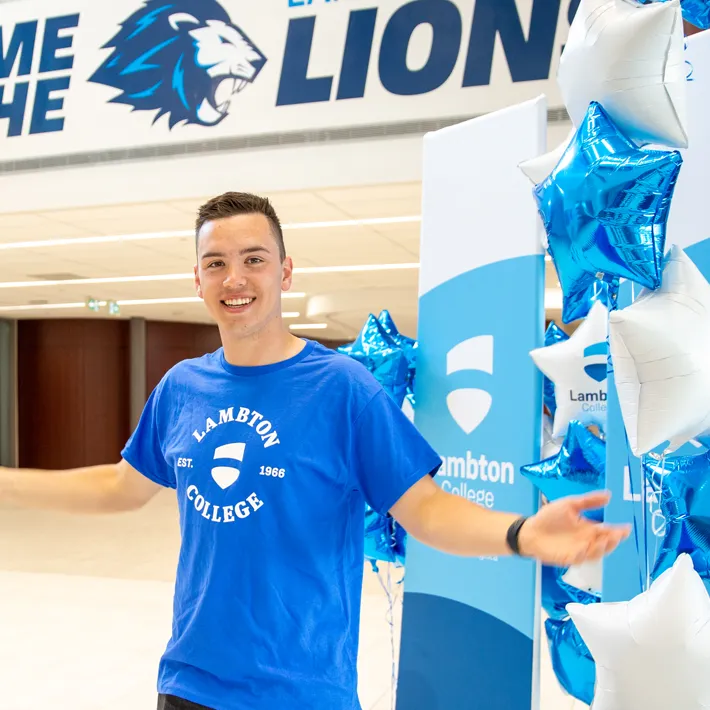 Student smiling in front of Lambton College banner and balloons