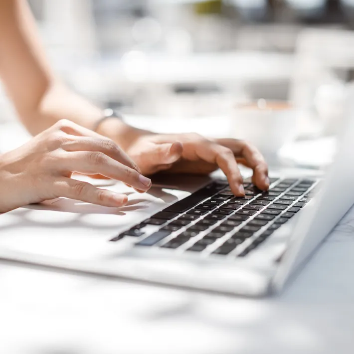 A closeup photo of hands typing on a computer, very bright and image with light features.