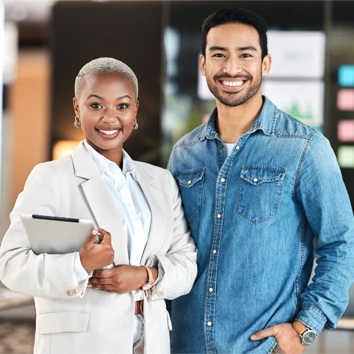 A stock photo of a man and women posing for photo in office setting.