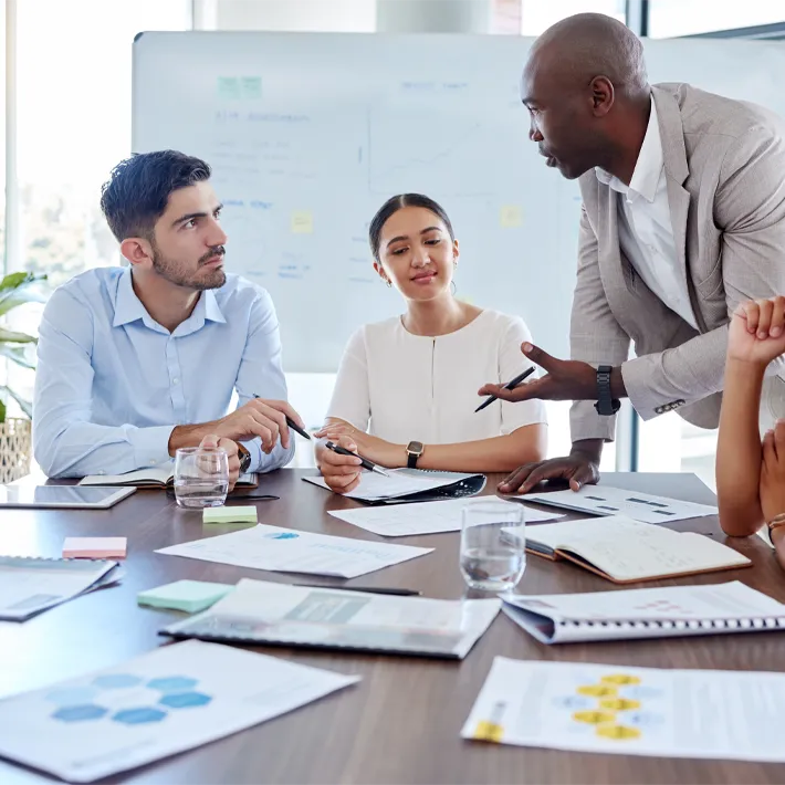 A group of employees sitting at a table planning with sheets of paper on desk.