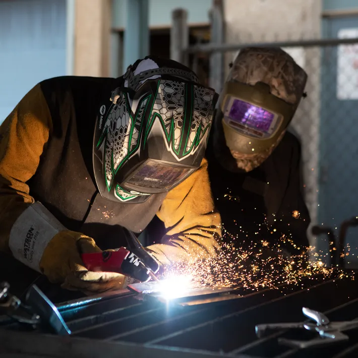 Two students in welding shop using tools with sparks flying.