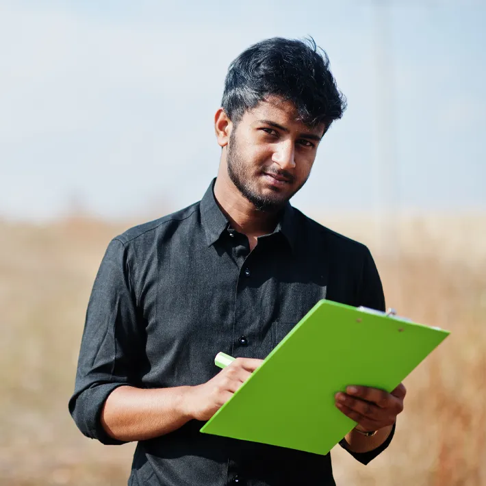 Argiculture student standing in feild with clipboard.