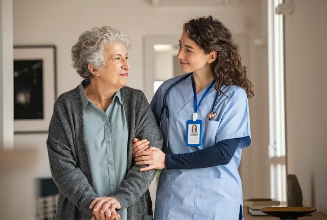 A long term care worker walking with a resident wearing blue scrubs.
