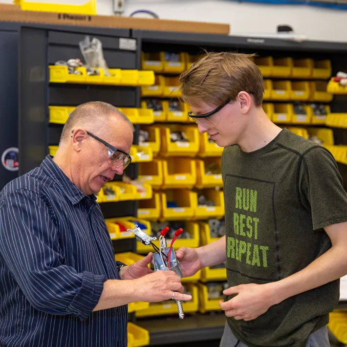 Highschool student going over electrical equipment with teacher in shop.