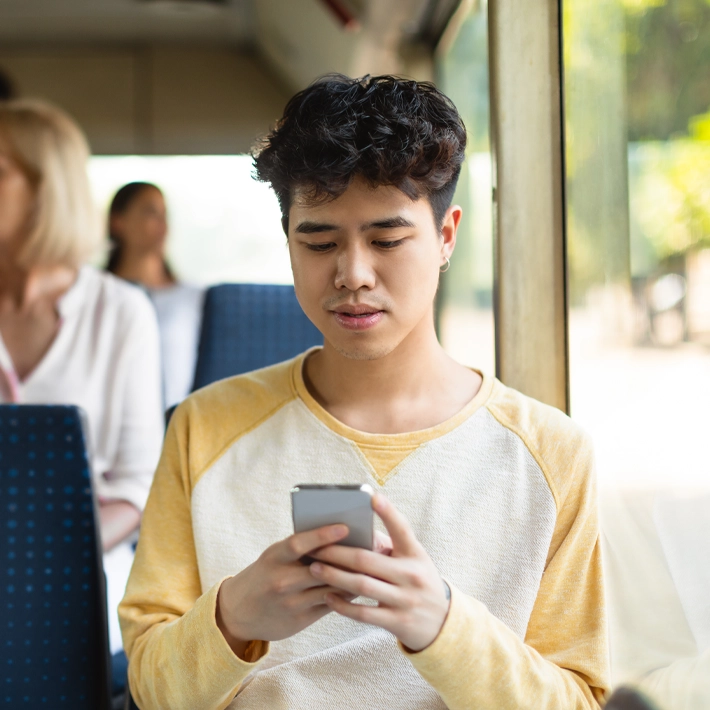 A photo of a young person on public transportation looking at his phone.