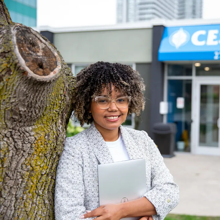 A woman international student posing for photo outside Cestar campus holding computer.