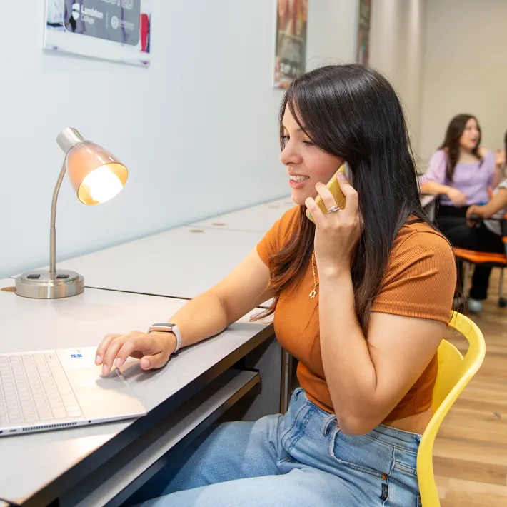 A lifestyle photo of a woman international student sitting at desk on campus on the phone.