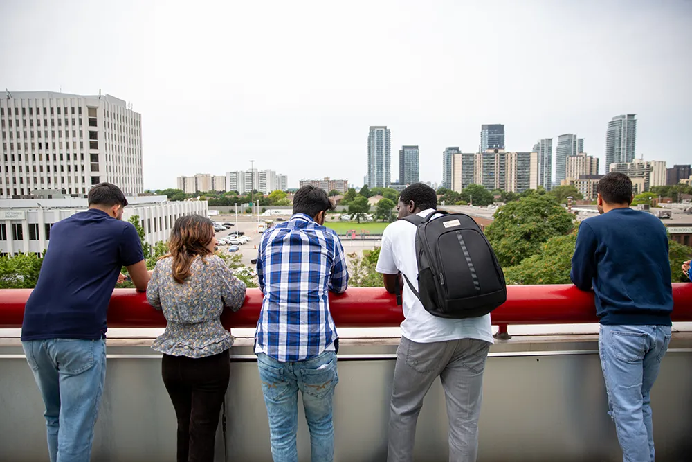 A group of international students looking at city on rooftop balcony area.