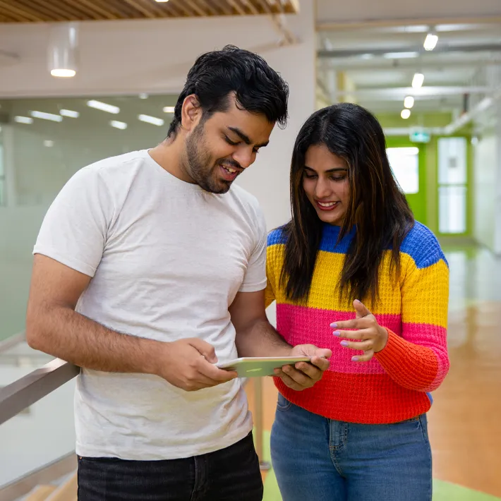 Two studenta (man and woman) looking at ipad while posing for photo on campus grounds.