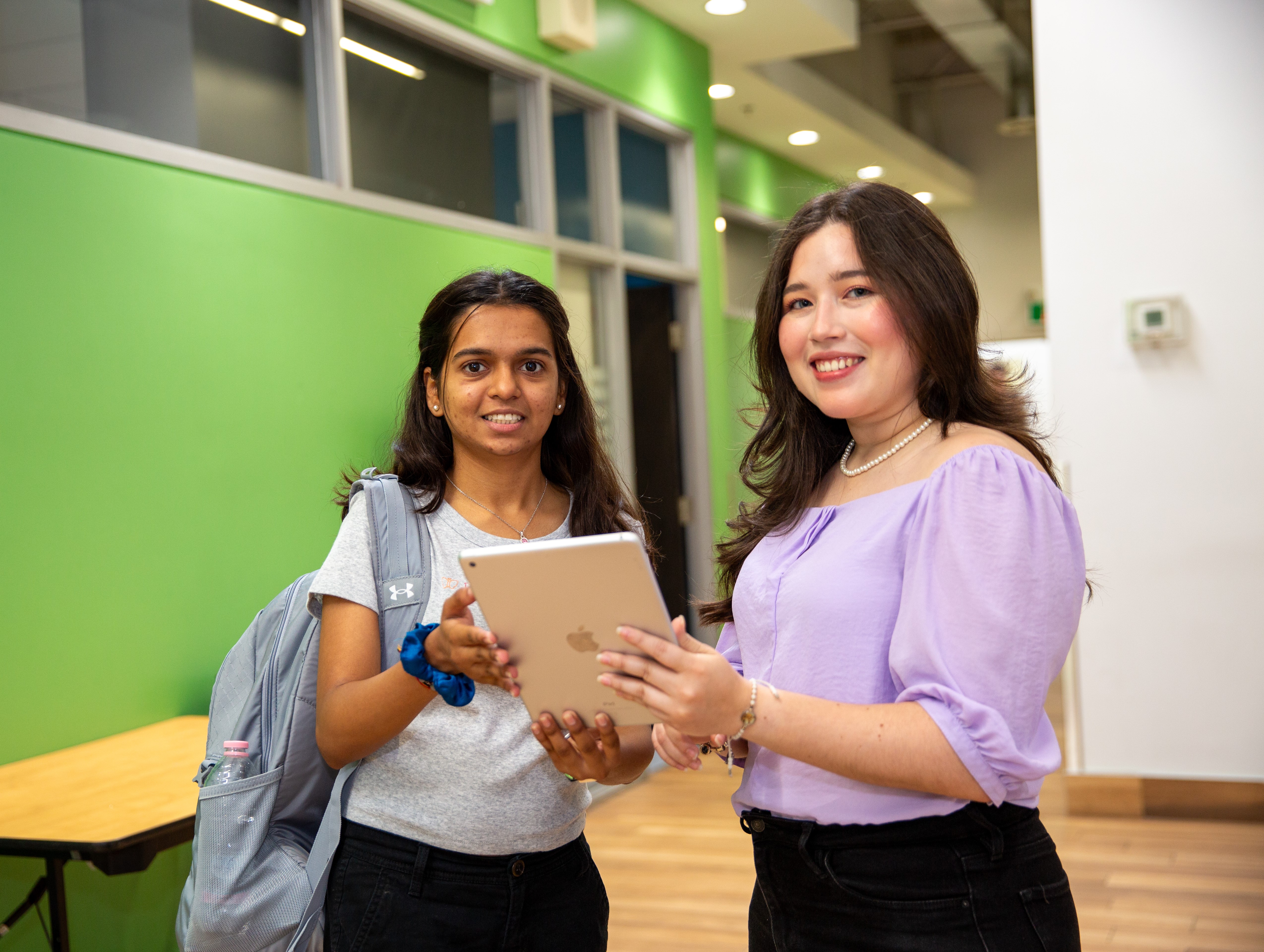 Two international students posing for photo on campus holding an ipad and smiling.