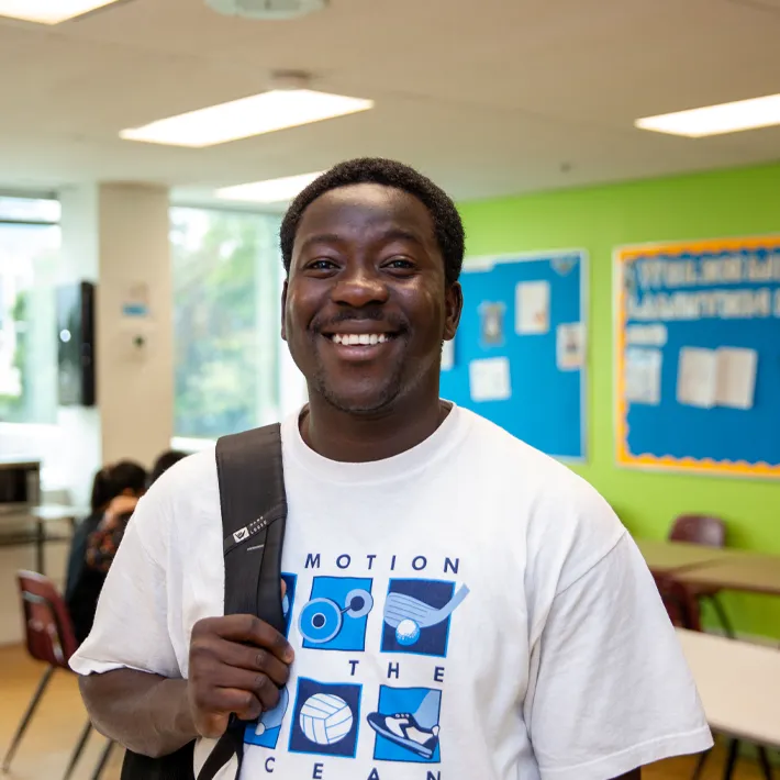 Cestar-Lifestyles-student-international A male international student wearing white graphic tshirt posing for photo in classroom with green wall.