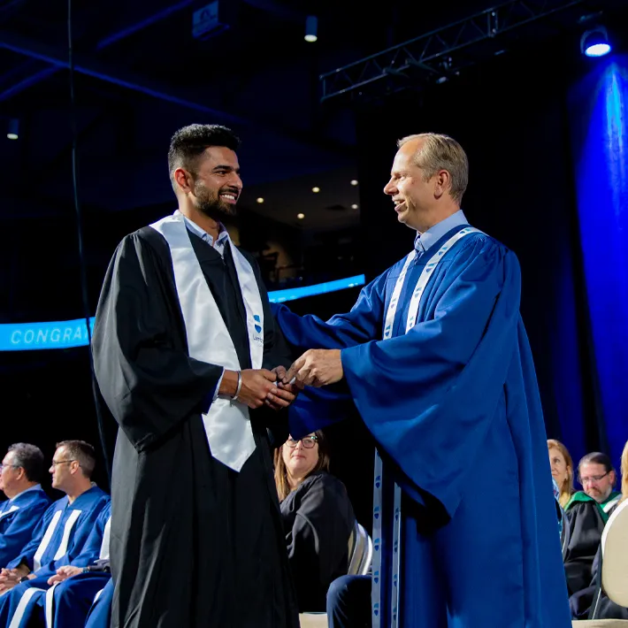 An international student on stage at the convocation ceremony shaking hands with lambton college professor.