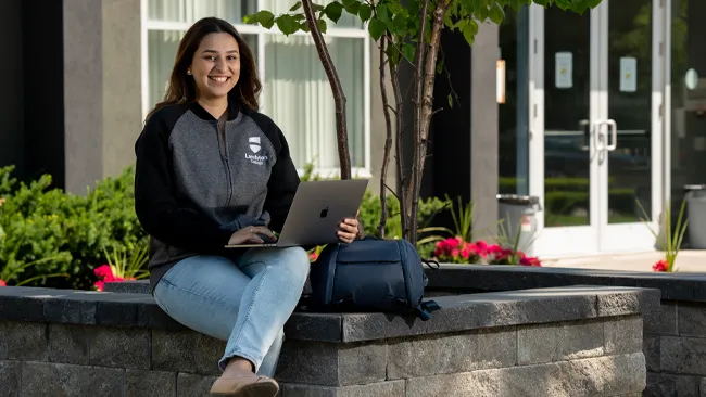 An international student sitting outside with computer.