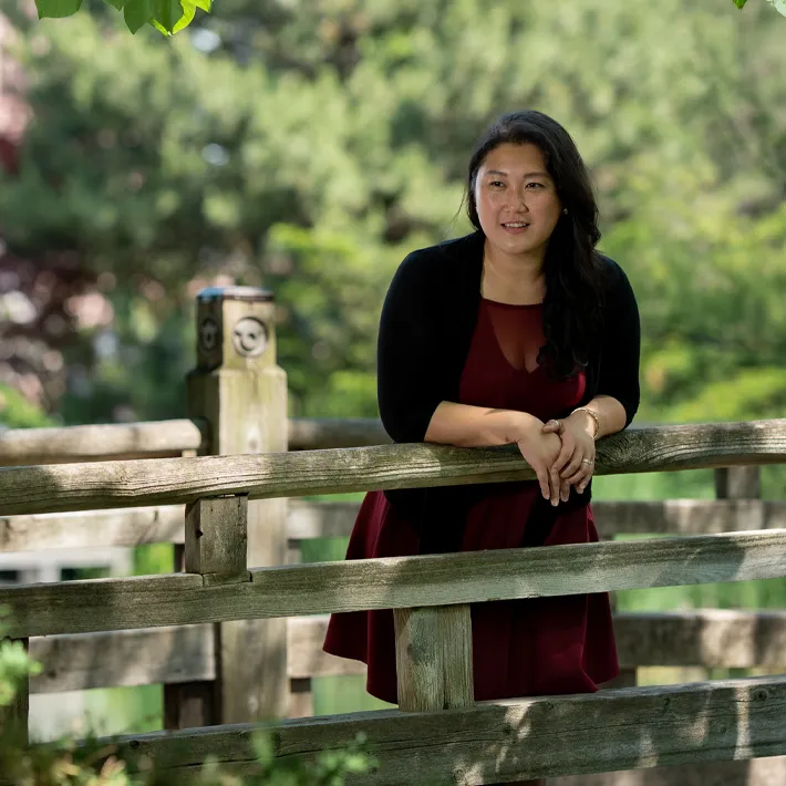 An international student leaning on fence outside of campus.