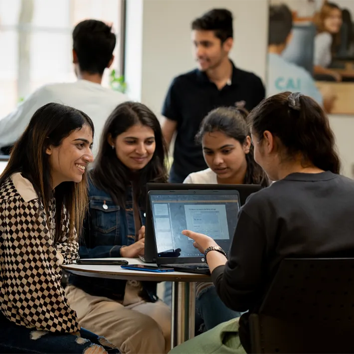 A group of international students sitting at a table working on project together with laptop.