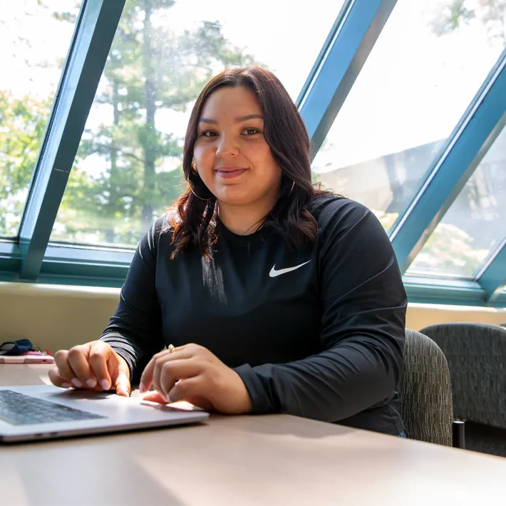 A photo of Jala George sitting at a desk in the common area on campus.