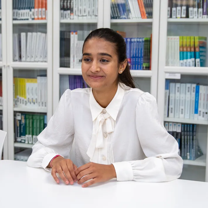 An international student sitting at desk with bookshelves behind her.