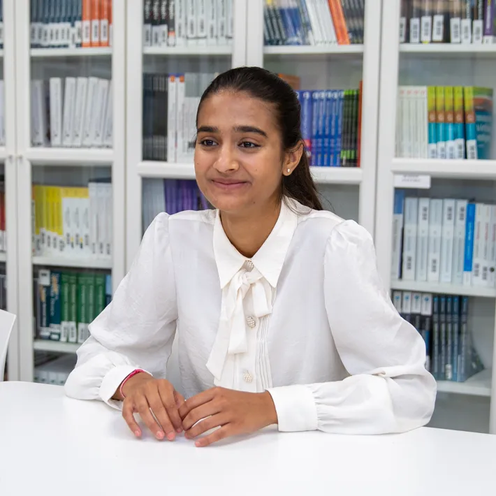 Queens-Lifestyles-mississauga-student An international student sitting at desk with bookshelves behind her.