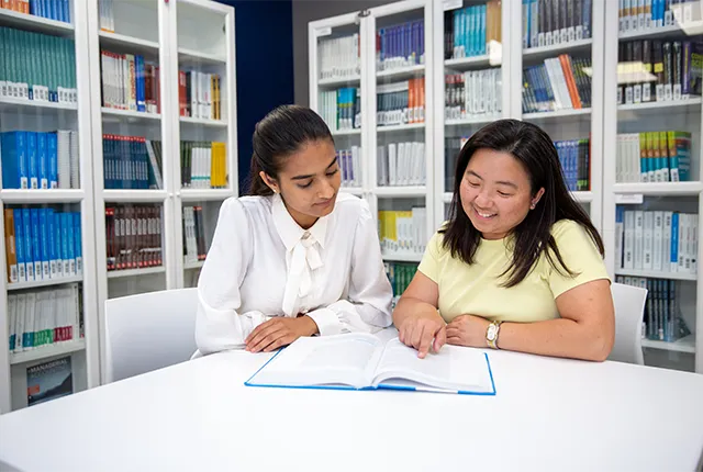 An image of two students stying in the common area with book shelves behind them.