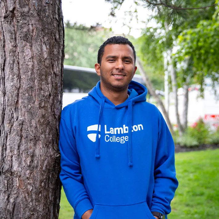 student-international A toronto international student wearing blue lambton college hoodie posing for photo outside.