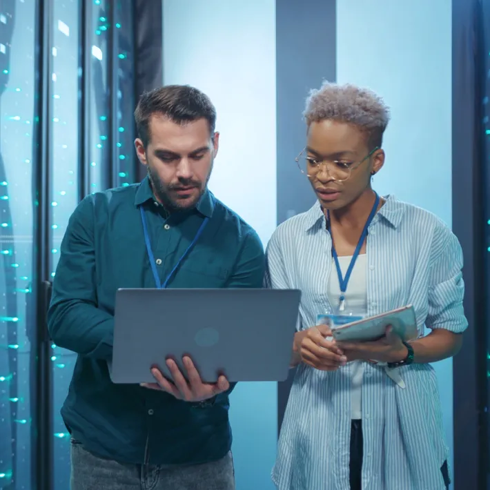 Two cyber security employees in data room looking at laptop.