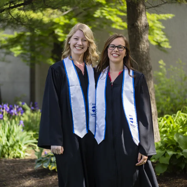 Two graduates posing for photos on college grounds.