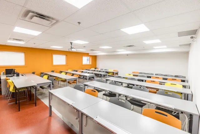 A photo of a classroom with an orange wlal and colourful chairs.