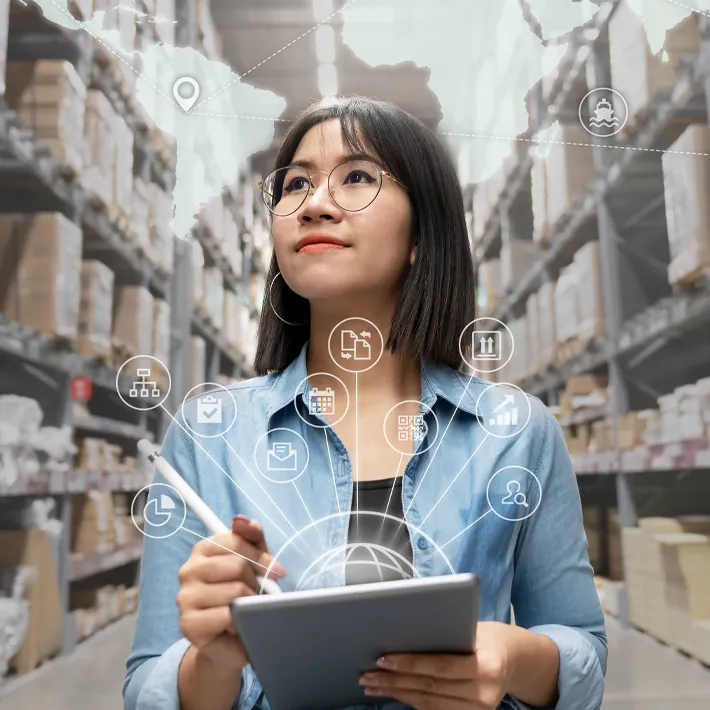A photo of a woman in a supply management building with boxes on shelves and holding ipad.