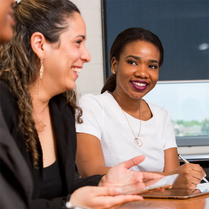 Business Internatonal students sitting at desk talking and smiling.