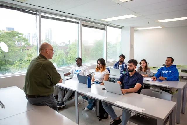 A photo of a classroom at the Toronto campus filled with students and a professor sitting at front of room.