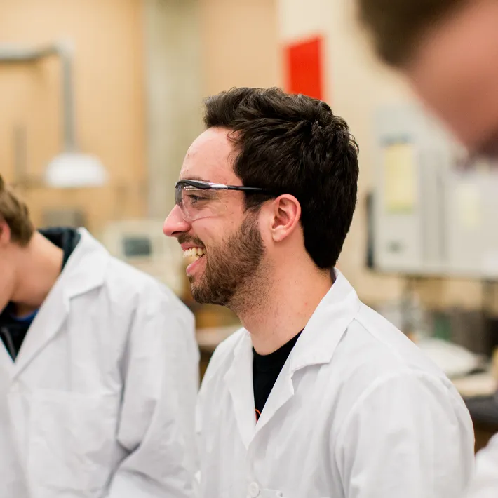 A student smiling in chemistry lab white coat on.