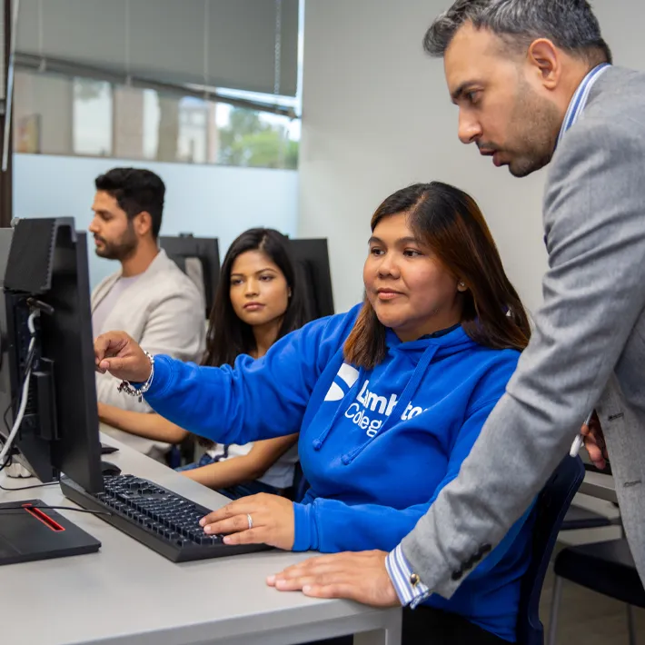 Three students sitting at computers with a teacher assissting them.