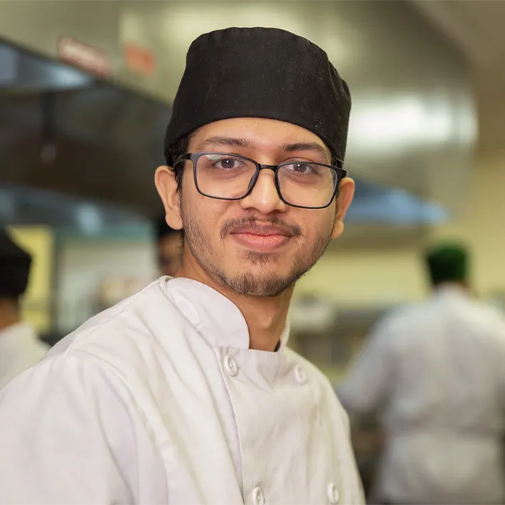 culx-pave-the-way-culinary-student A culinary student posing for photo in kitchen wearing white apron.