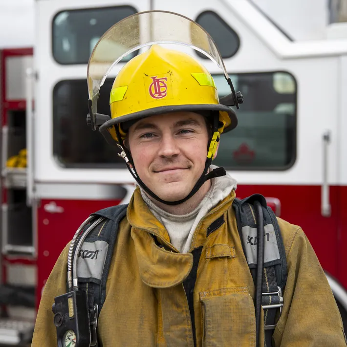 Fire student wearing gear standing in front of a fire truck.