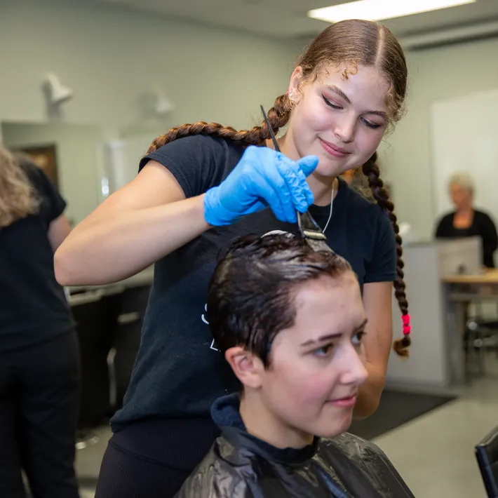 A hairstyling student practising dying hair on another student.