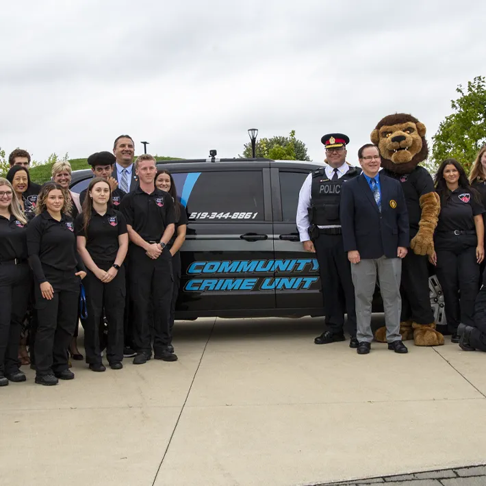Students and faculty posing for photo in front of Community Crime Unit van outside.