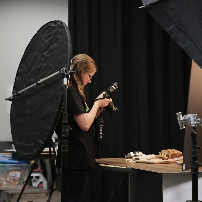 Photography student in studio taking photo of food on table.