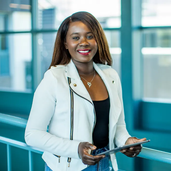 A student standing in hallway posing for photo and holding ipad.