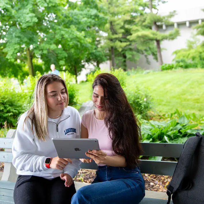 Students sitting on a bench outside in front of Lambton College