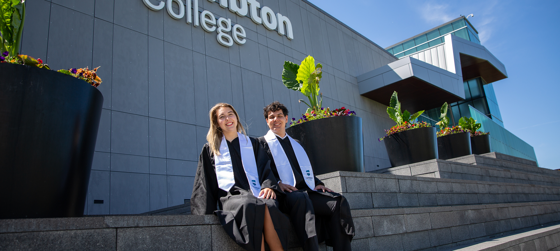 Two graduating convocation students sitting outside the building