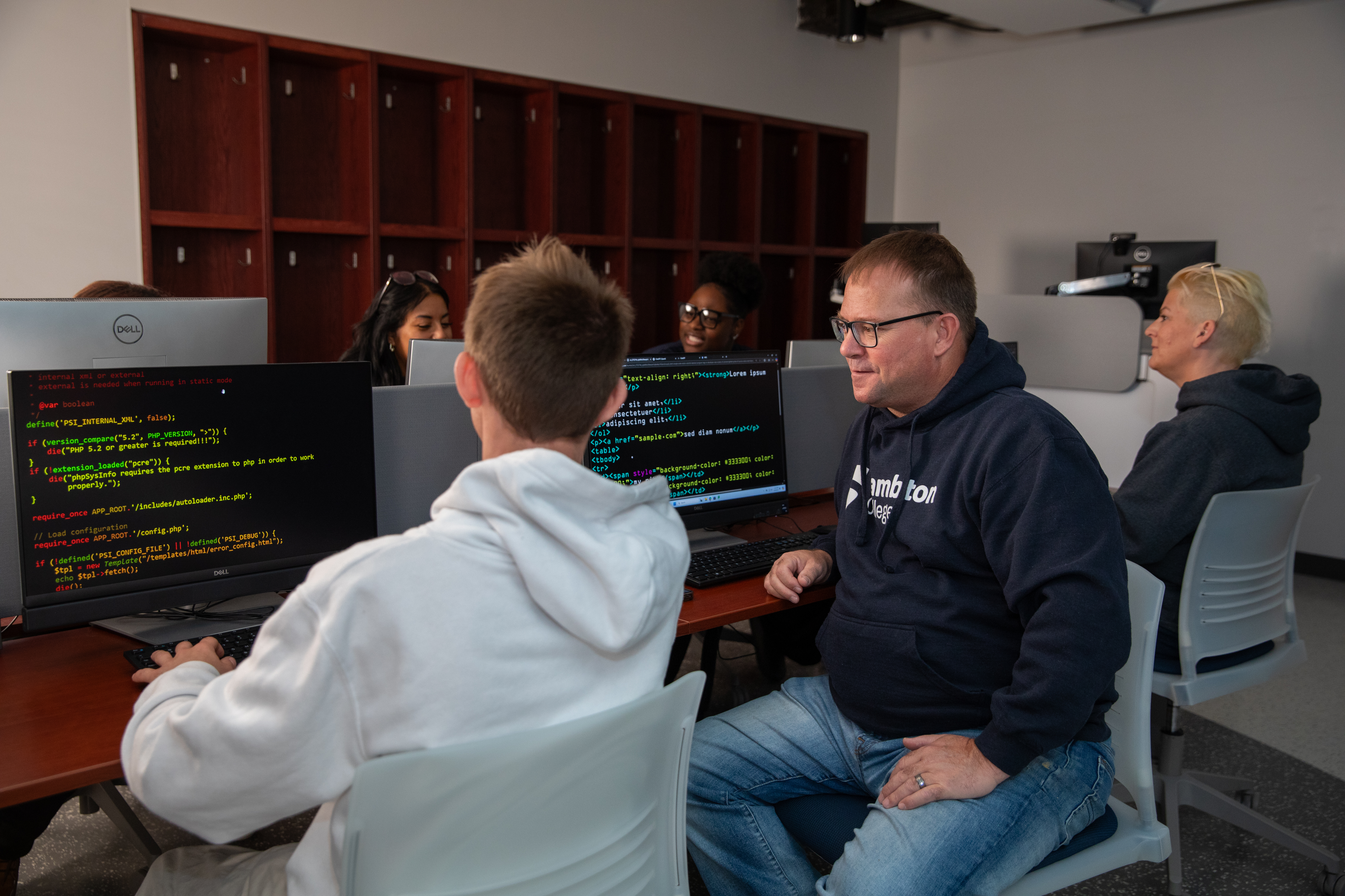 Two people sitting in a computer lab and discussing the code on the screen..
