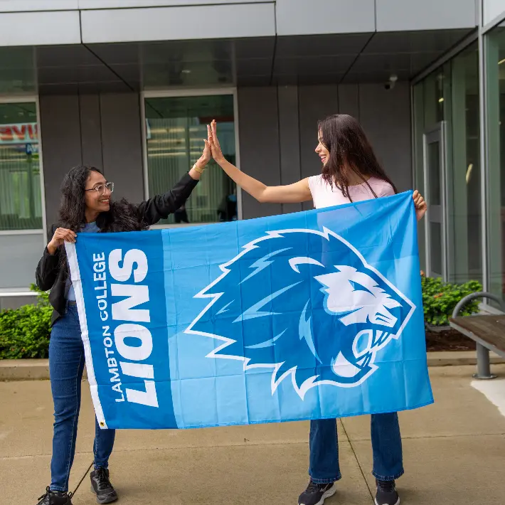 Two students holding the Lambton Lions flag and clapping hands