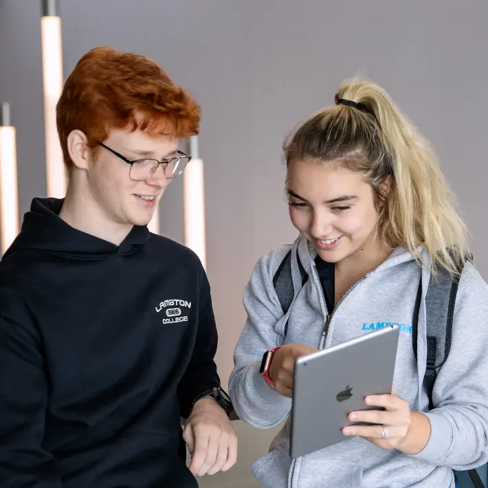 Two students in front of staircase looking at an iPad