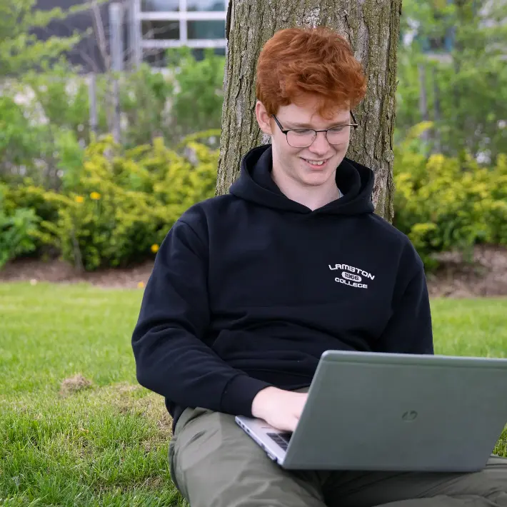 Student sitting outside amongst grass working on laptop